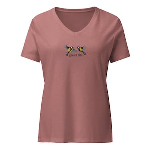 May include: Dusty rose V-neck t-shirt featuring an embroidered design of two yellow, black, and blue birds with outstretched wings. The text "great tits" is below the birds. A casual, short-sleeved top.