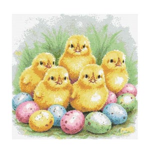 Puede incluir: Un grupo de seis pollitos amarillos rodeados de huevos de Pascua coloridos. Los pollitos están sentados en una cama de hierba verde.