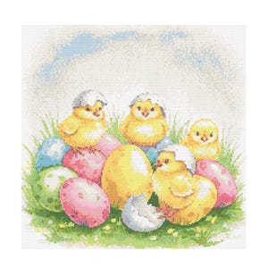 Puede incluir: Cinco pollitos amarillos con cáscaras blancas en la cabeza están acurrucados en una cama de hierba verde y huevos de Pascua coloridos. Los huevos son azules, verdes, rosas y amarillos.