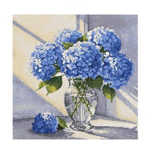 Puede incluir: Un ramo de hortensias azules en un jarrón de vidrio transparente con superficie texturizada. Las flores están dispuestas de forma suelta y natural y están iluminadas por un rayo de sol.