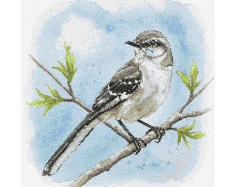 Könnte beinhalten: Ein Kreuzstich-Design eines Vogels, der auf einem Ast mit grünen Blättern sitzt. Der Vogel hat graue und weiße Federn, einen schwarzen Schnabel und ist vor einem hellblauen Aquarellhintergrund platziert. Der Ast ist braun und die Blätter sind ein leuchtendes Grün.