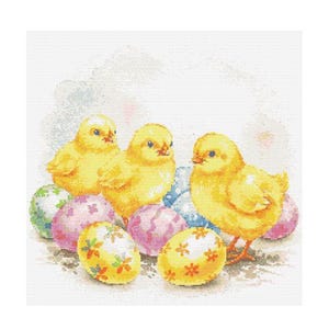 Puede incluir: Tres pollitos amarillos sentados sobre huevos de Pascua coloridos. Los pollitos se miran y los huevos están decorados con diferentes patrones.