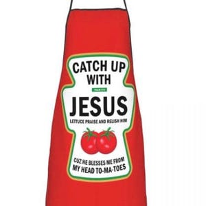 May include: Red apron with the text "CATCH UP WITH JESUS" in a white and green design. The apron also features the phrases "Lettuce praise and relish him" and "Cuz he blesses me from my head to-ma-toes".