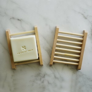 May include: Two wooden soap dishes. One dish has a bar of soap with the text "WE CRAFT SOAP" and a logo.