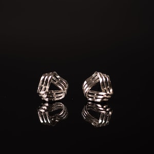 May include: A pair of silver earrings with a geometric design. The earrings are shaped like a triangle and have a woven pattern.