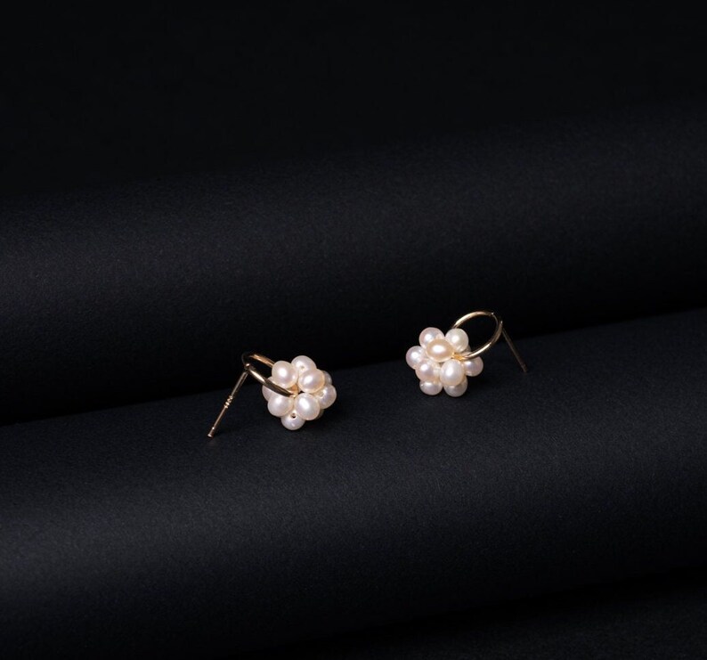Peut inclure: Une paire de boucles d'oreilles cr&eacute;oles en or avec un groupe de petites perles blanches. Les boucles d'oreilles sont sur une surface noire.