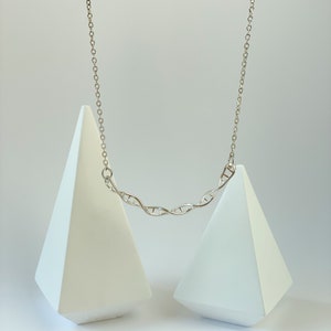 May include: A silver necklace with a DNA double helix pendant. The necklace is displayed on two white triangular stands.
