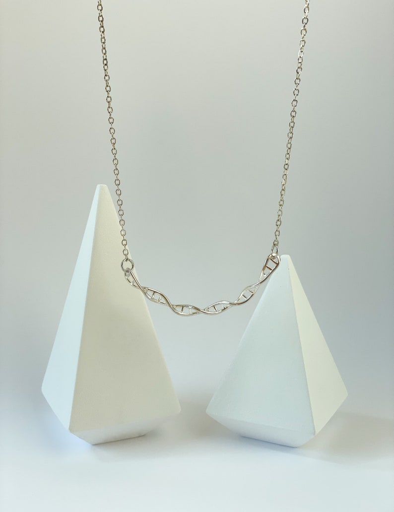 May include: A silver necklace with a DNA double helix pendant. The necklace is displayed on two white triangular stands.