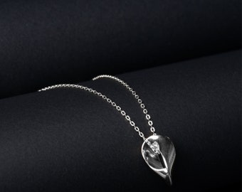 May include: A silver necklace with a delicate chain and a pendant shaped like a leaf with a small diamond in the center.