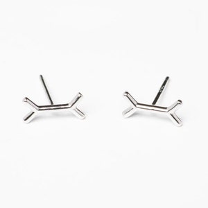 May include: A pair of silver stud earrings with a geometric design. Each earring features a small, abstract shape that resembles a stylized letter X.