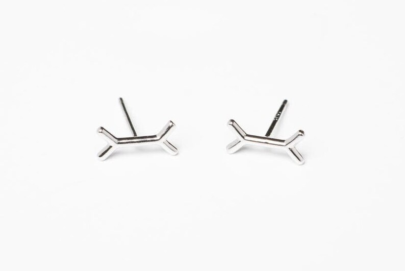 May include: A pair of silver stud earrings with a geometric design. Each earring features a small, abstract shape that resembles a stylized letter X.
