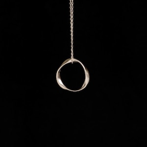 Puede incluir: Un collar con colgante plateado con un diseño de círculo abierto y retorcido. El colgante cuelga de una fina cadena sobre un fondo negro. La joya es sencilla y elegante, adecuada para el uso diario.