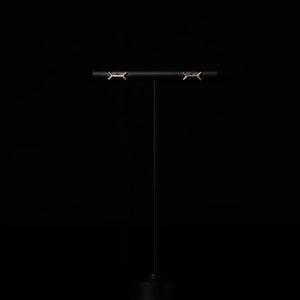 May include: A pair of silver earrings with a geometric design, displayed on a black stand against a black background.