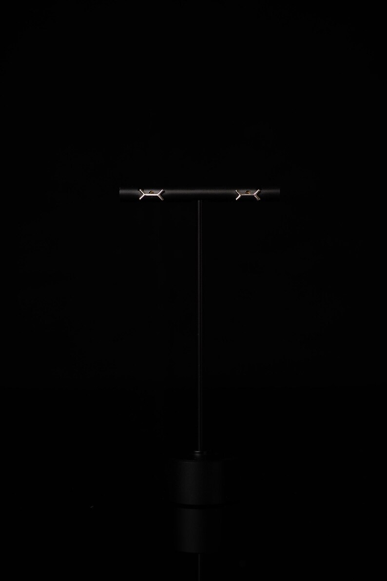 May include: A pair of silver earrings with a geometric design, displayed on a black stand against a black background.