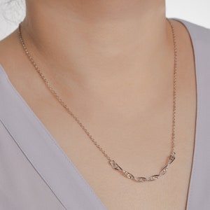 May include: A silver chain necklace with a delicate, interlocking design. The chain is thin and has a subtle shine.