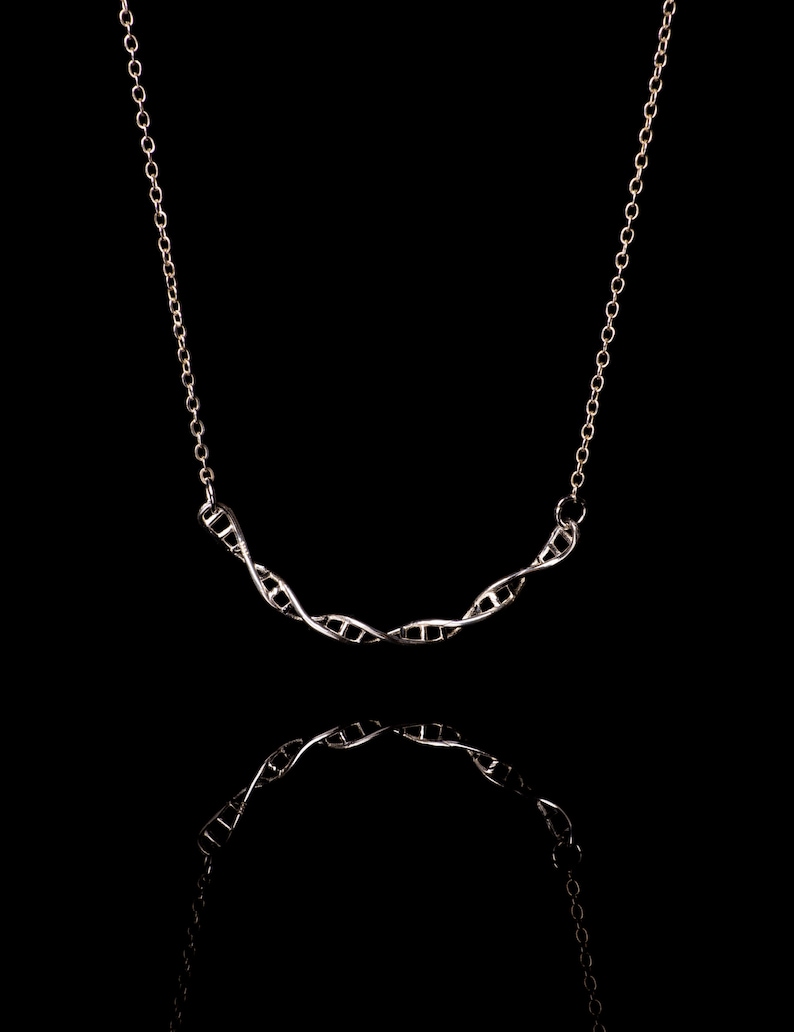May include: A silver necklace with a double helix pendant, a symbol of DNA, against a black background.
