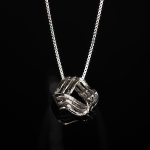 Puede incluir: Un collar de cadena de plata con un colgante de plata que tiene un diseño abstracto retorcido.