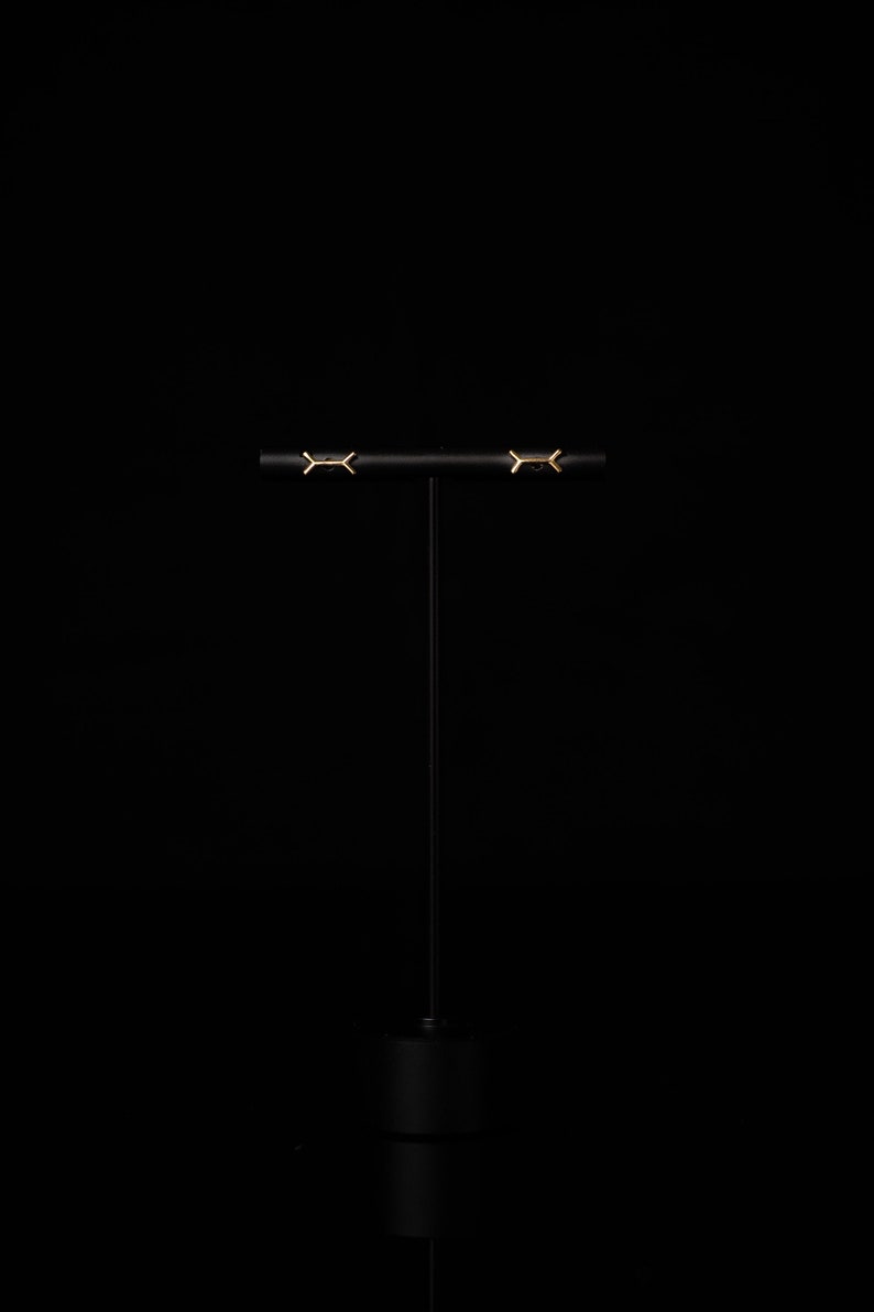 May include: A pair of gold earrings with a geometric design, displayed on a black stand.