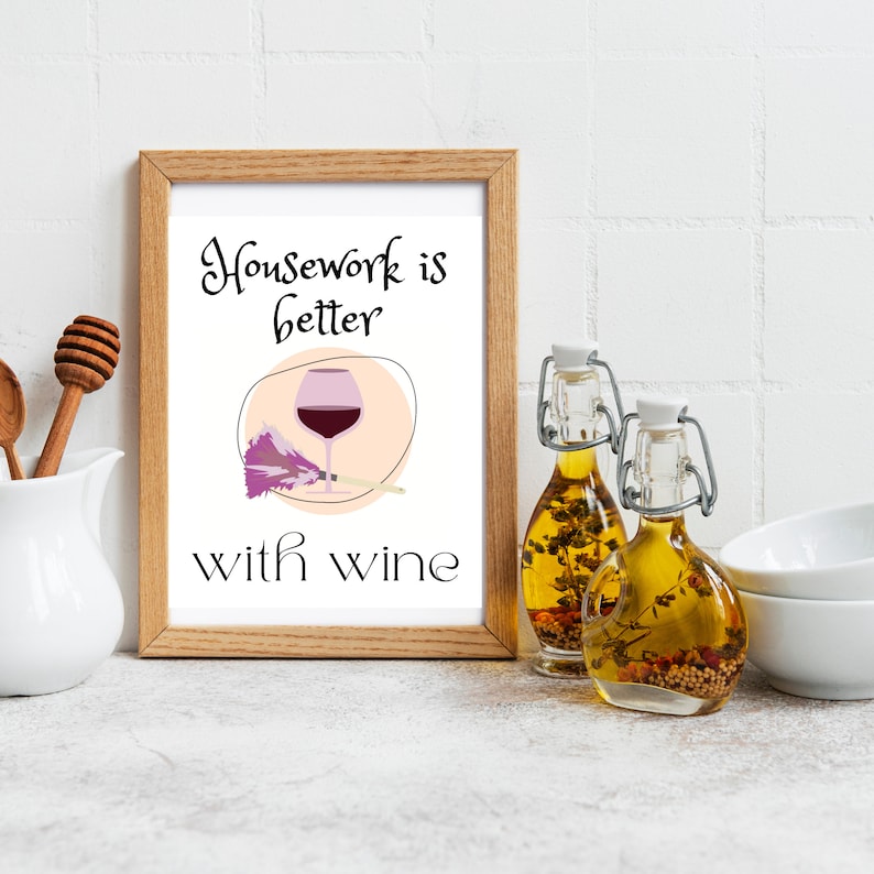 Picture in frame that says "housework is better with wine," with a wine glass with red wine in it and purple feather duster next to it.