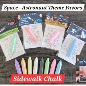 May include: Space-themed party favors with a rocket ship design. Each favor includes a small piece of sidewalk chalk and a coloring page. The text on the favor says "Blast Off!" and "Lift Off!"