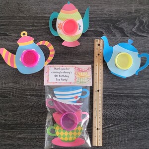 May include: A set of tea party favor bags with a thank you tag that reads "Thank you for coming to Avery's 4th Birthday Tea Party!" The bags contain a stack of teacups with a pink lid and a blue teapot with a pink lid.