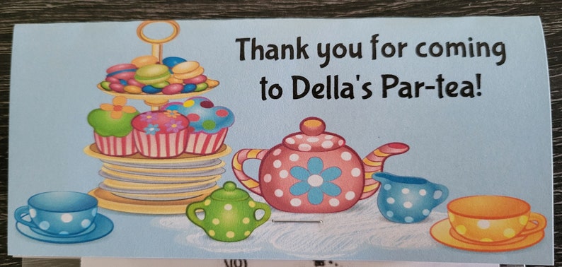 May include: A blue and white thank you card with the text "Thank you for coming to Della's Par-tea!"  The card features a teapot, teacups, and a tiered cake stand with cupcakes and macarons.