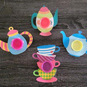 May include: Four colorful teacups and teapots with lids, decorated with floral patterns and hearts. Each teapot and teacup has a small, round, clear container for holding slime or playdough.