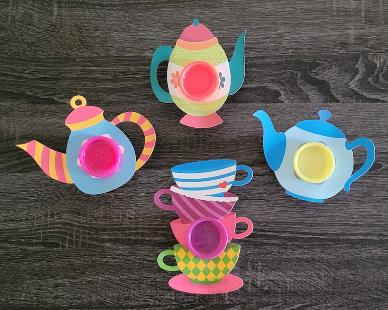May include: Four colorful teacups and teapots with lids, decorated with floral patterns and hearts. Each teapot and teacup has a small, round, clear container for holding slime or playdough.