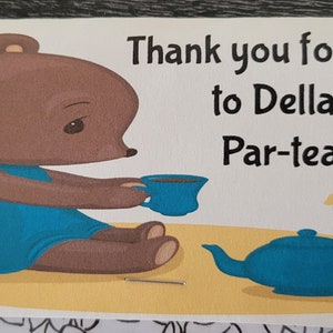 May include: Thank you for coming to Della's Par-tea! A brown bear wearing a blue dress sits at a table with a teapot and a cup of tea.