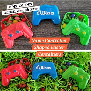 May include: Three plastic Easter egg containers shaped like game controllers. The containers are red, blue, and green. The blue container has the name "Atticus" written on it. The containers are filled with colorful jelly beans and green grass.