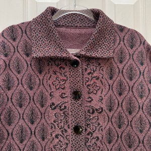Puede incluir: Un c&aacute;rdigan morado con un estampado floral negro y rosa. El c&aacute;rdigan tiene un cierre de botones y un cuello.