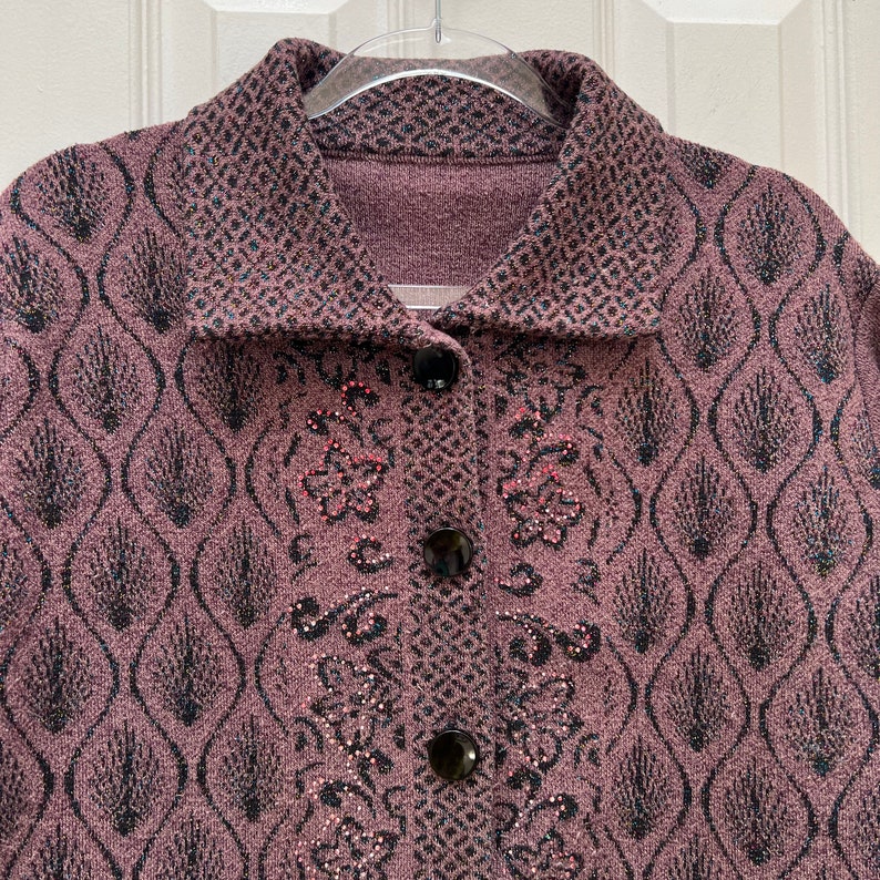 Puede incluir: Un c&aacute;rdigan morado con un estampado floral negro y rosa. El c&aacute;rdigan tiene un cierre de botones y un cuello.