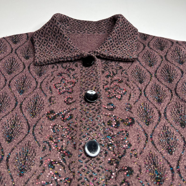 Puede incluir: Un c&aacute;rdigan marr&oacute;n con un dise&ntilde;o estampado en blanco y negro. El c&aacute;rdigan tiene cuello y botones. La tela tiene una textura brillante.