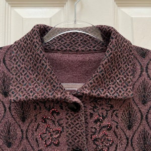 Puede incluir: Un c&aacute;rdigan marr&oacute;n con un dise&ntilde;o estampado en blanco y negro. El c&aacute;rdigan tiene cuello y cierre de botones. El c&aacute;rdigan est&aacute; adornado con pedrer&iacute;a.