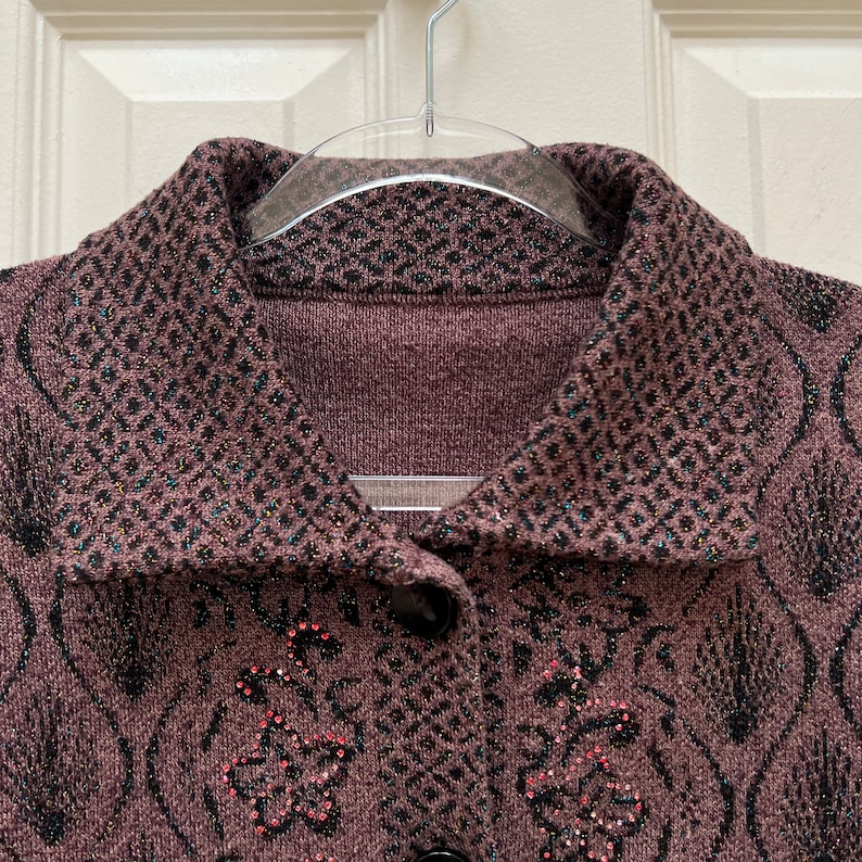 Puede incluir: Un c&aacute;rdigan marr&oacute;n con un dise&ntilde;o estampado en blanco y negro. El c&aacute;rdigan tiene cuello y cierre de botones. El c&aacute;rdigan est&aacute; adornado con pedrer&iacute;a.