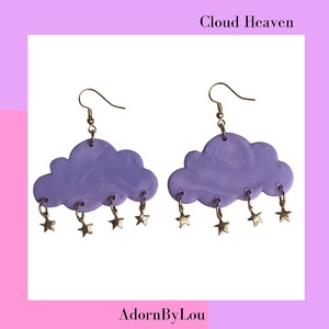 Peut inclure: Boucles d'oreilles en forme de nuage violet avec des breloques étoiles dorées. Les boucles d'oreilles sont étiquetées "Cloud Heaven" et "AdornByLou".