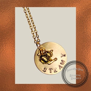 Op de afbeelding: Gouden ketting met een ronde hanger waarop "STEAMY" staat en een klein gouden theepot-bedeltje.