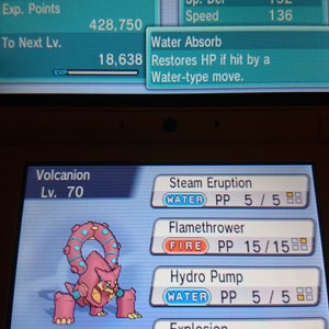 Pode incluir: Um personagem Pokémon Volcanion rosa e azul na tela de um videogame. O Pokémon é de nível 70 e tem os movimentos Erupção de Vapor, Lança-chamas, Hidrobomba e Explosão. O Pokémon está usando um Colete de Assalto.