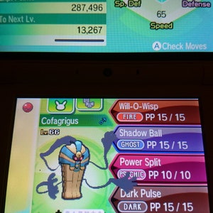 May include: A screen displays a Cofagrigus character from a video game. The character is a tan, blue, and gold mummy-like figure. The screen shows stats, moves, and other game information.