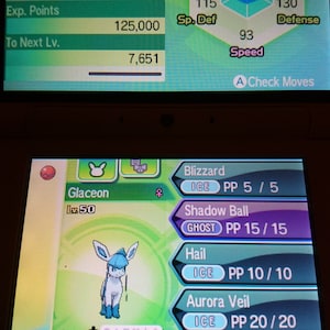 Pode incluir: Um dispositivo de jogos portátil exibe o perfil de um Pokémon Glaceon. A tela mostra estatísticas, movimentos como Blizzard e Bola Sombra, e habilidades. O Pokémon do tipo gelo Glaceon é retratado em azul e branco.