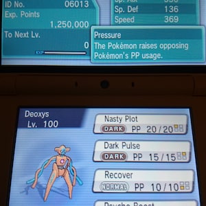 May include: A screenshot of a Nintendo DS game showing a Deoxys Pokémon at level 100. The Pokémon is a Psychic type and has the Pressure ability. The Pokémon's stats are shown, as well as its moves: Nasty Plot, Dark Pulse, Recover, and Psycho Boost.
