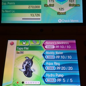 May include: A screenshot of a video game showing a Tapu Fini Pokemon with a level of 60. The Pokemon is a Water and Fairy type with a blue and white colour scheme. The Pokemon's stats are displayed, including its HP, attack, defence, special attack, special defence, and speed. The Pokemon's moves are also displayed, including Nature's Madness, Muddy Water, Aqua Ring, and Hydro Pump.