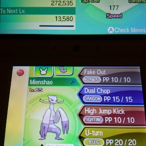 Pode incluir: Uma captura de tela de um videogame com um Pokémon chamado Mienshao. A tela mostra as estatísticas do Pokémon, incluindo HP, Ataque e Velocidade, junto com seus movimentos. A interface do jogo é visível.