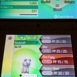 Pode incluir: Uma captura de tela de um jogo Nintendo 3DS mostrando um Pokémon Rockruff com o texto "Rockruff Lv. 10" e uma lista de movimentos: Tackle, Mordida, Presa de Fogo e Hora Feliz.