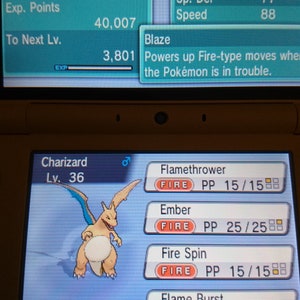 May include: A Nintendo 3DS screen displays a Charizard Pokémon with stats and moves. The Charizard is level 36, with Fire and Flying types. The screen shows the moves Flamethrower, Ember, Fire Spin, and Flame Burst.
