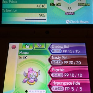 Pode incluir: Uma captura de tela de um jogo Nintendo 3DS mostrando um Pokémon chamado Hoopa, nível 15, dos tipos Psíquico e Fantasma. Hoopa é uma criatura roxa e rosa com um anel dourado em torno de sua cabeça. A tela mostra as estatísticas, os movimentos e as habilidades de Hoopa. Os movimentos são Bola Sombra, Trama Maligna, Psíquico e Buraco do Hiperespaço. A habilidade é Mágico e o item é Faixa de Foco.