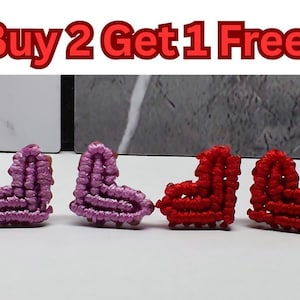 May include: Four heart-shaped macrame earrings. Two are a light purple colour, and the other two are red. The text "Buy 2 Get 1 Free" is at the top of the image.