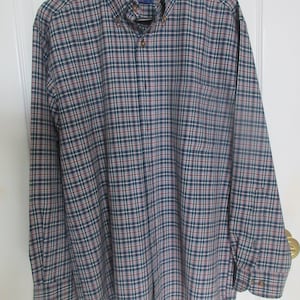 May include: A long-sleeved plaid button-down shirt in blue, red, and white. The shirt has a pocket on the left side and the brand name "Periglon" is visible on the tag.