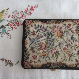 Puede incluir: Una caja vintage de punto de aguja floral con borde negro. La caja está llena de una variedad de flores y hojas coloridas.