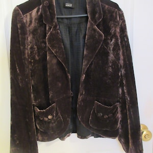 Puede incluir: Una chaqueta de terciopelo marrón con cuello de muesca, dos bolsillos y cierre de botón. La chaqueta tiene una etiqueta que dice "STEFAN SCHRODT".